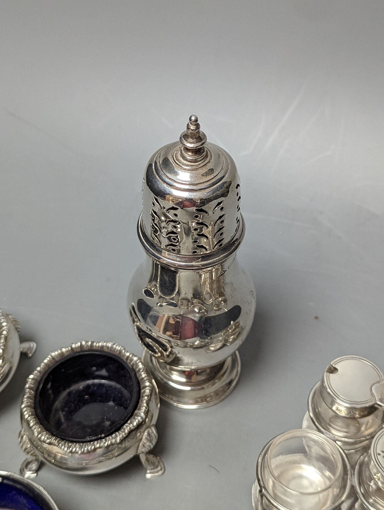 A late Victorian small silver condiment stand with three glass condiments, London, 1883, 49mm, other minor condiments and a silver sugar caster.